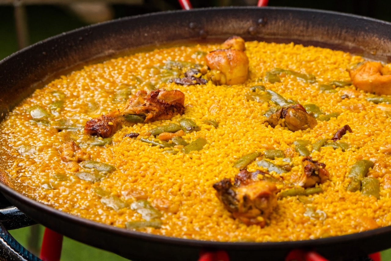 Close-up of paella valenciana with chicken and flat green beans, the rice still bubbling in the pan