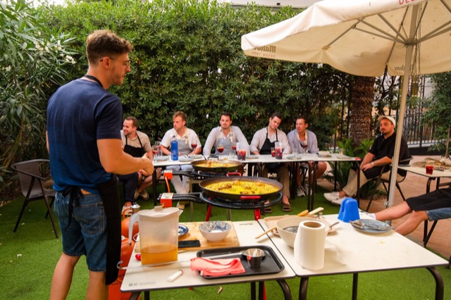 The cook talking a table of guests through each step during a paella workshop in a Valencia garden