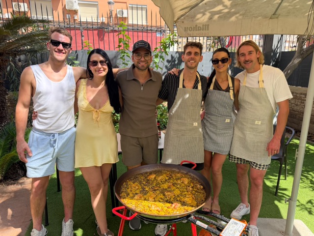 Group in striped aprons posing behind the paella they cooked